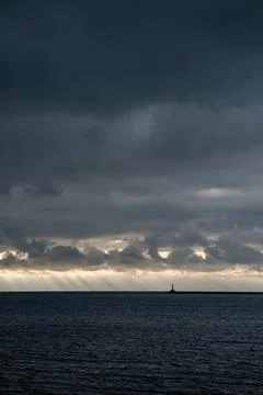 Lighthouse silhouette with sun rays over dark sea Stock Photos