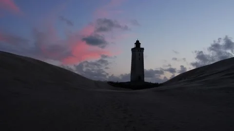 Lighthouse standing between sand dunes during sunset Stock Footage 338124693