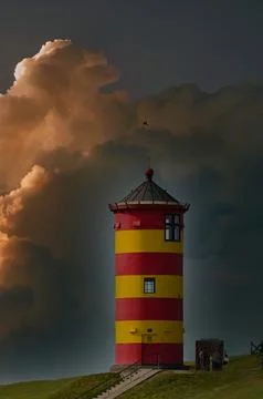 Lighthouse stands on a hill under dark clouds during sunset in a coastal area Stock Photos