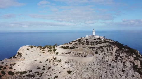 A lighthouse stands on rocky cliffs with a view of the vast sea and a cloudy Stock Footage 340532946