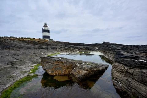 Lighthouse surrounded by rocks with moss and reflections in the water. Wexfor Stock Photos