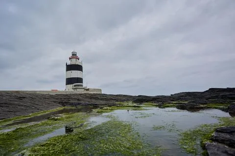 Lighthouse surrounded by rocks with moss and reflections in the water. Wexfor Stock Photos