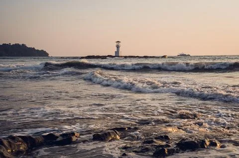 Lighthouse surrounded by water and cloudy sunset sky Stock Photos