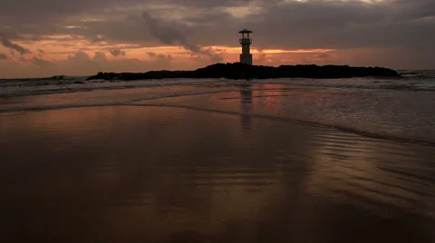 Lighthouse  with waves washing sandy beach at sunset. Stock Footage 68430622