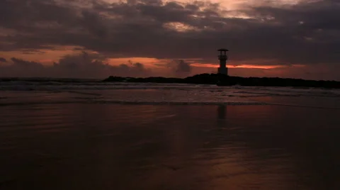 Lighthouse  with waves washing sandy beach at sunset. Stock Footage 68452528