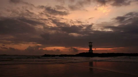 Lighthouse  with waves washing sandy beach at sunset. Stock Footage 68452618