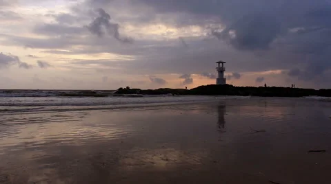 Lighthouse  with waves washing sandy beach at sunset. Stock Footage 68452662