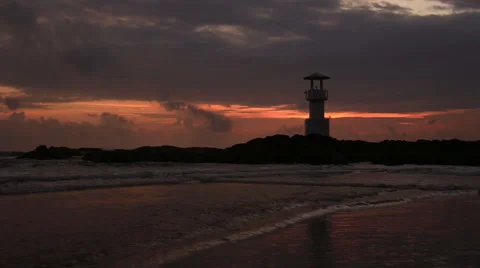 Lighthouse  with waves washing sandy beach at sunset. Stock Footage 68452668