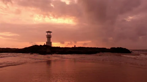 Lighthouse  with waves washing sandy beach at sunset. Stock Footage 68452787