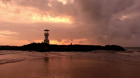 Lighthouse  with waves washing sandy beach at sunset. Stock Footage 68452851