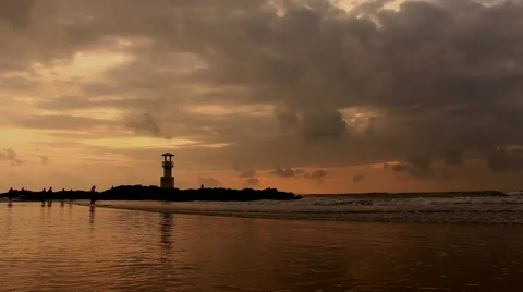 Lighthouse  with waves washing sandy beach at sunset. Stock Footage 68452856