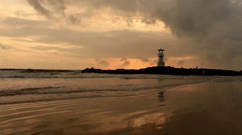 Lighthouse  with waves washing sandy beach at sunset. Stock Footage 68452871