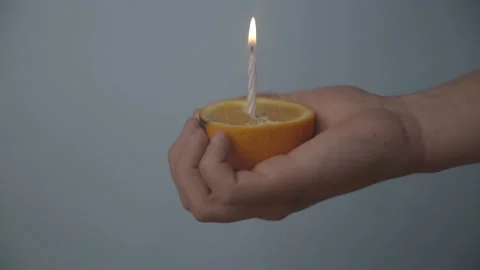 Lighting a Candle in an Orange and Squeezing The Orange, Blue Background LOG Stock Footage 136992478
