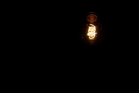 Lighting decor. Hanging Light Bulb in the dark room with copy space. Stock Photos