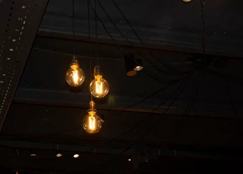 Lighting decor. Hanging Light Bulb in the dark room with copy space. Stock Photos