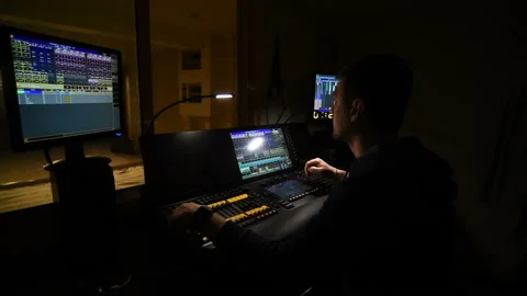 Lighting engineer works on a light console in his office overlooking the theater Stock Footage 155080503