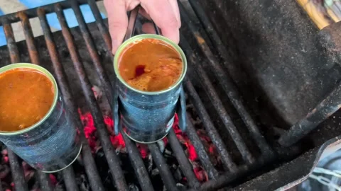 Lighting a fire and cooking canned goulash soup and pouring it up in bowls with Stock Footage 331301430