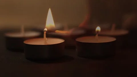 Lighting a group of small tea light candles with a match in a dark cozy room Video stock 338193222