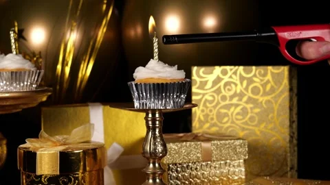 Lighting a Single Candle on a Cupcake with Gold Presents and Balloons in the Stock Footage 345197470