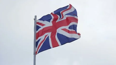 Lightly battered British flag waving in wind on gray sky background, Union Flag Stock Footage 206811776