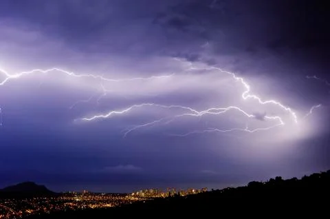 A lightning storm over a city in a valley. Forks of lightening emerging from Stock Photos