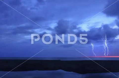 A lightning storm over the ocean. Forks of lightening emerging from clouds. Stock Photos