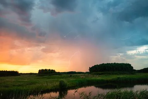 Lightning storm over river meadow with thunderclouds and reflective water Stock Photos