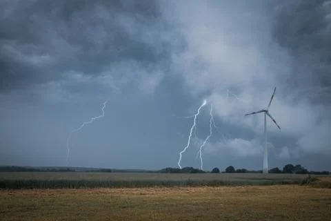 A lightning strikes the ground next to a wind turbine Stock Photos