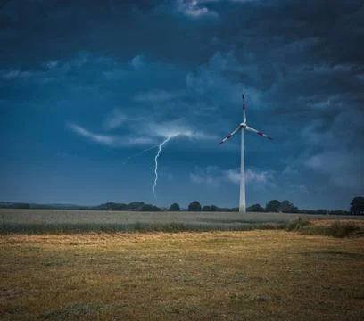 A lightning strikes the ground next to a wind turbine Stock Photos