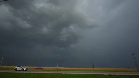 Lightning striking beneath massive dark storm clouds over rural highway with Stock Footage 335958989