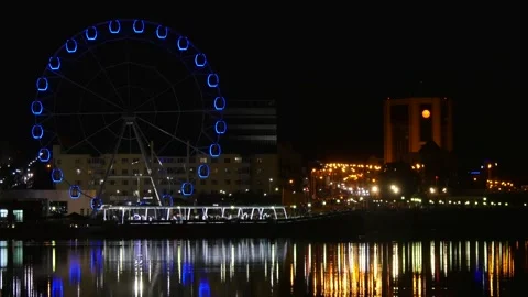 The lights of the large Ferris wheel are reflected in the water of the bay. Stock Footage 282869131