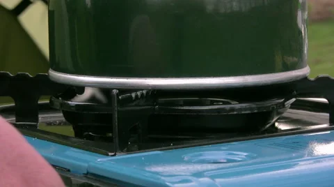 Lightweight camping kettle is on a lit single ring butane gas camping stove Stock Footage 50458077