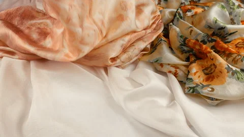 Lightweight plain silk scarf falls gently onto a pile of floral fabrics. Video stock 337406127