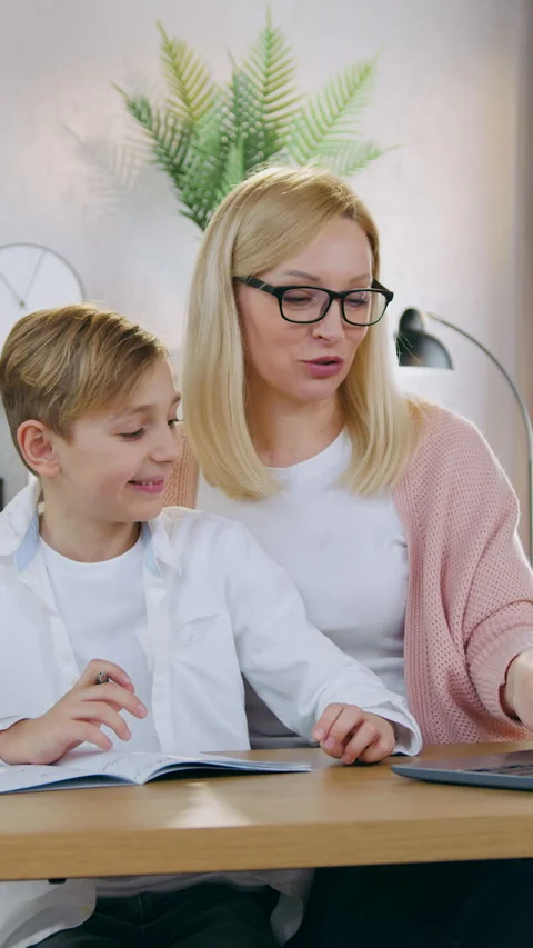 Likable surprised 12-aged boy sitting in front of computer together with his ado Stock Footage 331206008