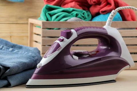 Lilac iron and a stack of clothes in a box on a natural wooden background. ir Foto stock