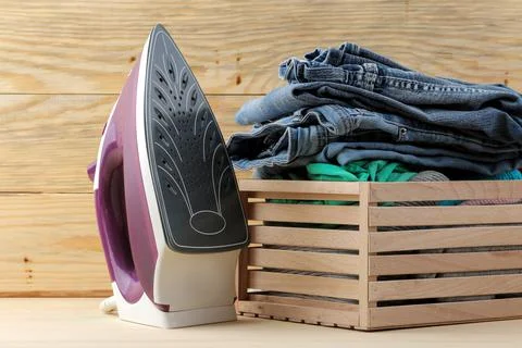 Lilac iron and a stack of clothes in a box on a natural wooden background. ir Stock Photos