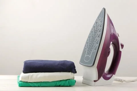 Lilac iron and a stack of clothes on a light background. ironing clothes. hou Stock Photos