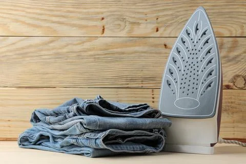 Lilac iron and a stack of jeans on a natural wooden background with place for Stock Photos