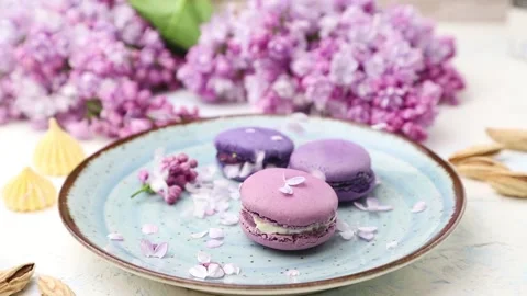 Lilac petals falling on a ceramic plate with purple macaroons. Stock Footage 131865836