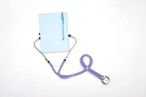 A lilac phonendoscope lies on a table with a notepad and a pen, view from above Stock Photos