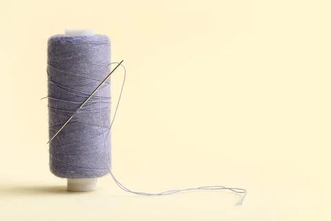 Lilac sewing thread with needle on beige background Stock Photos
