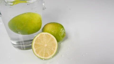 A lime in half dropped into a glass of water splash with a whole lime Stock Footage 88512280