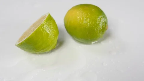 A lime in half dropped onto a white background rolling next to a whole lime Stock Footage 88512190
