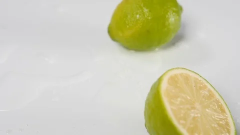 A lime in half rolling in water on a white background next to a whole lime Stock Footage 88512059