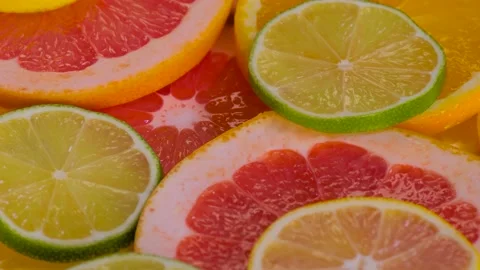 Lime, orange, grapefruit and lemon fruit slices on rotating surface - close up Stock Footage 231189759