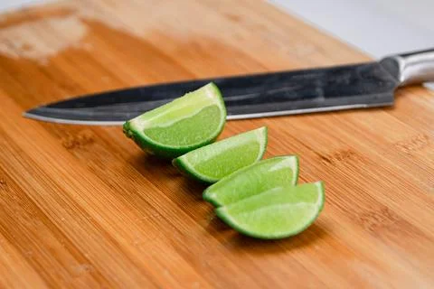 A lime sliced in quarters and placed on a wooden cutting board next to knife. Stock Photos