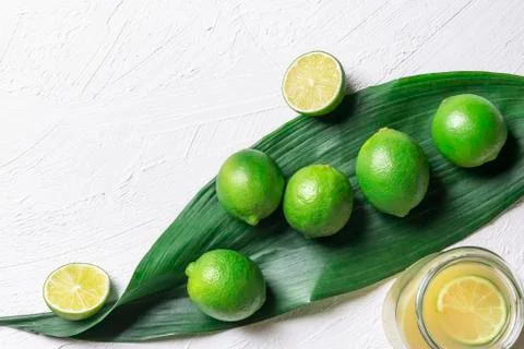 Limes on a big leaf and jar with juice. Fresh green citrus fruits. Healthy fo Stock Photos