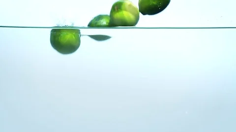 Limes dropping into water on blue background in slow motion. Stock Footage 76553056