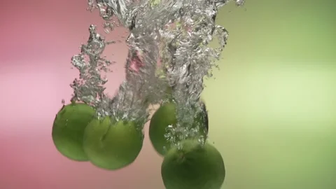 Limes fall into water in slow motion. on a colored background Stock Footage 131037021