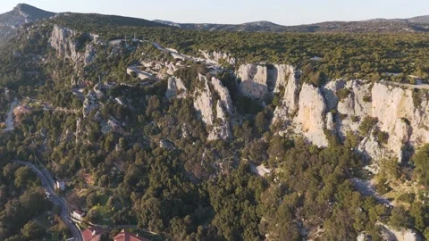 Limestone cliffs above forested hillside near Baunei with winding road 库存影片 334787478